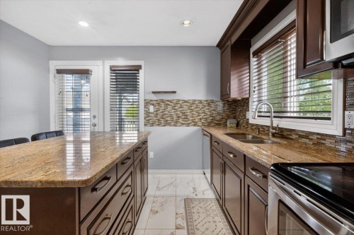 Kitchen featuring a center island, wood-finish cabinetry, stone countertops, and tile backsplash - 946 Jordan Crescent, Edmonton, AB 