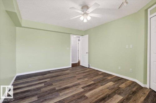 Spacious room featuring multi-toned wood-finish flooring, light green walls, a white ceiling fan with integrated lighting, and white baseboards - 946 Jordan Crescent, Edmonton, AB 
