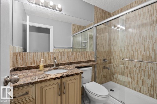 Bathroom featuring a glass-enclosed shower, decorative tile surround, wood-finish vanity with stone countertop, and an integrated sink with a chrome faucet - 946 Jordan Crescent, Edmonton, AB 