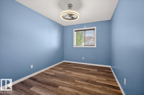 Room featuring wood-finish flooring, blue painted walls, a window with blinds, and an overhead light fixture - 946 Jordan Crescent, Edmonton, AB 
