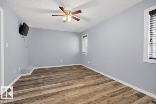 Spacious room featuring wood-finish flooring, two windows with blinds, a ceiling fan, and light grey walls - 946 Jordan Crescent, Edmonton, AB 