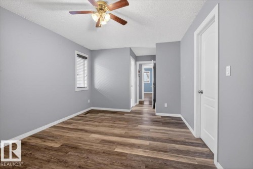 Spacious room featuring wood-finish flooring, light gray walls, a window with horizontal blinds, a ceiling fan with integrated lighting, and white trim throughout - 946 Jordan Crescent, Edmonton, AB 
