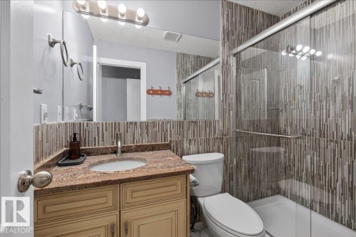 Bathroom featuring a glass-enclosed shower, a vanity with a stone-finish countertop, and a built-in wall mirror - 946 Jordan Crescent, Edmonton, AB 