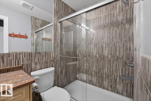 Contemporary bathroom featuring a glass-enclosed shower with sliding door, vertical mosaic tile surround, and a coordinating vanity with a stone countertop - 946 Jordan Crescent, Edmonton, AB 