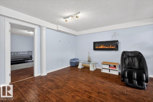 Living area featuring wood-finish flooring, light blue wall paint, and a mounted electric fireplace - 946 Jordan Crescent, Edmonton, AB 