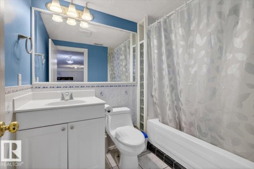 Bathroom featuring a white vanity with integrated sink, a large wall-mounted mirror, a standard toilet, and a shower-tub combination with glass block detailing - 946 Jordan Crescent, Edmonton, AB 