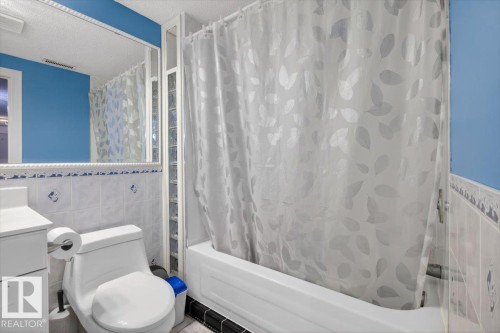 Bathroom featuring a white vanity, wall-mounted mirror with decorative trim, white ceramic tile, and a built-in bathtub with glass block partition - 946 Jordan Crescent, Edmonton, AB 