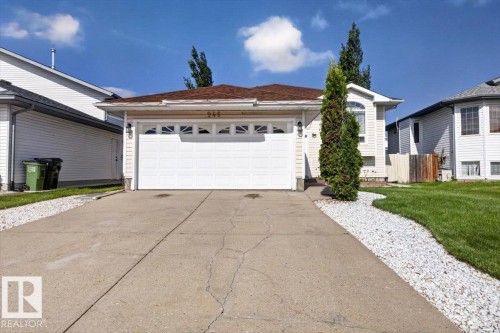 Front exterior featuring a two-car garage with a panel door, a concrete driveway, and a decorative white stone pathway - 946 Jordan Crescent, Edmonton, AB 