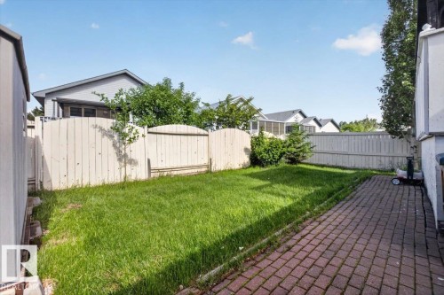 Fenced backyard featuring a paver patio, a lush lawn, a storage shed, and established perimeter trees - 946 Jordan Crescent, Edmonton, AB 
