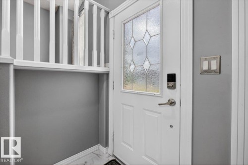Entry door with decorative leaded glass paneling, smart lock hardware, and brushed nickel handle - 946 Jordan Crescent, Edmonton, AB 