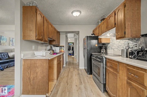 Galley kitchen featuring wood-finish cabinetry, light-toned countertops, a stainless steel range, and wood-finish flooring - 45 2020 105 Street, Edmonton, AB 