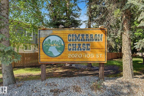 Cimarron Chase signage on wood-finish posts, set against a backdrop of mature evergreen and deciduous trees - 45 2020 105 Street, Edmonton, AB 