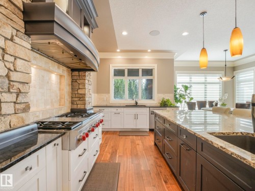 Gourmet kitchen featuring a stone-clad range hood, professional-grade gas range, wood-finish flooring, light-toned stone countertops, and a central island with a built-in sink - 2807 Wheaton Drive, Edmonton, AB 