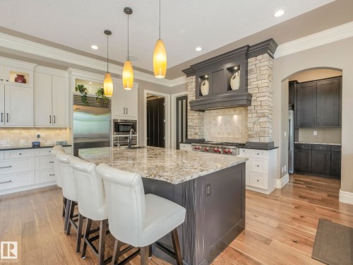 Spacious kitchen featuring a large central island with seating, stone-clad range hood, stainless steel appliances, light-toned cabinetry, and wood-finish flooring - 2807 Wheaton Drive, Edmonton, AB 