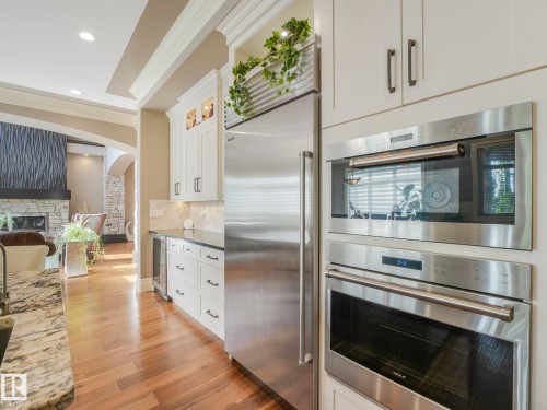 Gourmet kitchen with stainless steel appliances, built-in wall oven and microwave, white cabinetry, dark countertops, and wood-finish flooring - 2807 Wheaton Drive, Edmonton, AB 