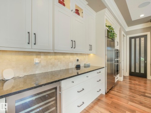 White shaker cabinetry with dark hardware, dark stone countertops, a tiled backsplash, and wood-finish flooring - 2807 Wheaton Drive, Edmonton, AB 