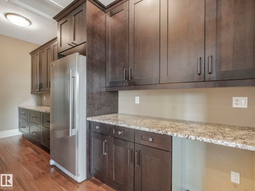 Stainless steel refrigerator integrated into dark wood cabinetry with granite-style countertops - 2807 Wheaton Drive, Edmonton, AB 