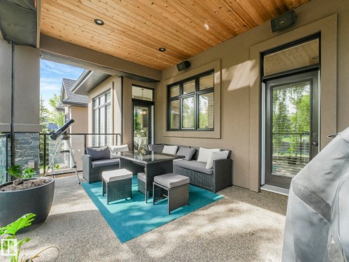 Covered outdoor patio featuring a wood-panel ceiling with recessed lighting, exposed aggregate flooring, and a stone-clad pillar - 2807 Wheaton Drive, Edmonton, AB 