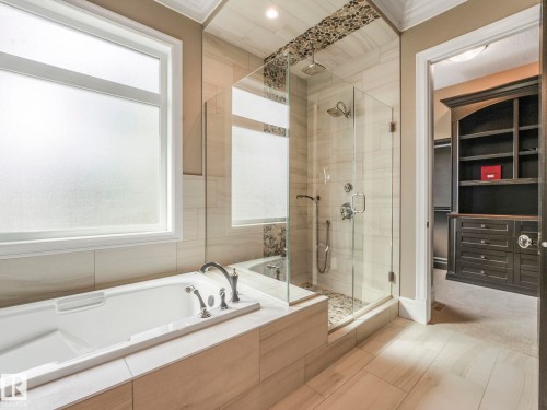 Bathroom featuring a freestanding tub with deck-mounted fixtures, a glass-enclosed shower with a rainfall showerhead and pebble-tile floor, and large format wall and floor tiling - 2807 Wheaton Drive, Edmonton, AB 