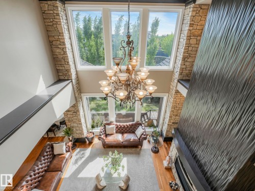 Two-story living area featuring a prominent chandelier, stone-clad fireplace surround with textured wall paneling, and a wood-finish floor - 2807 Wheaton Drive, Edmonton, AB 
