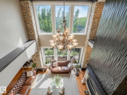 Two-story living area featuring a prominent chandelier, stone-clad fireplace surround with textured wall paneling, and a wood-finish floor - 