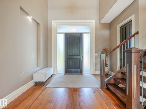 Foyer entry with wood-finish flooring, a contemporary dark wood door with frosted sidelights and transom, an illuminated wall niche, and a staircase featuring wood newel posts and metal balusters - 2807 Wheaton Drive, Edmonton, AB 