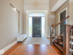 Foyer entry with wood-finish flooring, a contemporary dark wood door with frosted sidelights and transom, an illuminated wall niche, and a staircase featuring wood newel posts and metal balusters - 