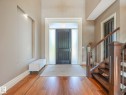 Foyer entry with wood-finish flooring, a contemporary dark wood door with frosted sidelights and transom, an illuminated wall niche, and a staircase featuring wood newel posts and metal balusters - 2807 Wheaton Drive, Edmonton, AB 