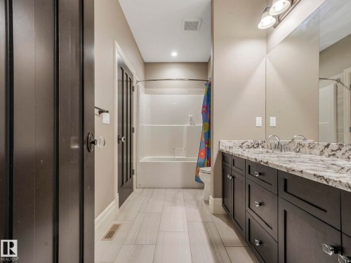 Spacious bathroom featuring a dual vanity with a patterned stone countertop, dark wood cabinetry, and a full-width mirror - 2807 Wheaton Drive, Edmonton, AB 