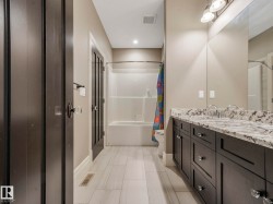 Spacious bathroom featuring a dual vanity with a patterned stone countertop, dark wood cabinetry, and a full-width mirror - 