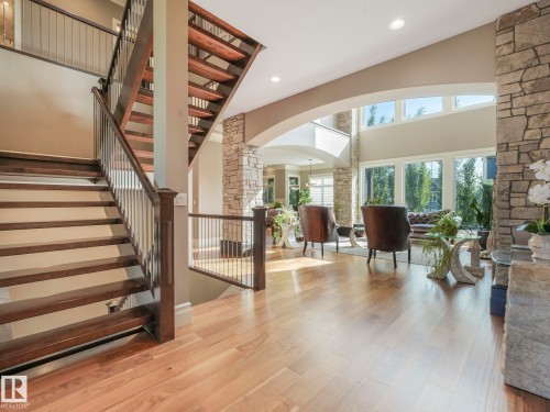 Two-story entryway featuring wood-finish flooring, a grand staircase with dark wood treads and metal balusters, and a stone accent wall - 2807 Wheaton Drive, Edmonton, AB 