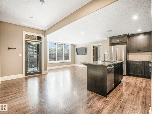 Open-concept kitchen and living area featuring wood-finish flooring, a kitchen island with a basin sink, stainless steel appliances, and dark wood cabinetry - 2807 Wheaton Drive, Edmonton, AB 