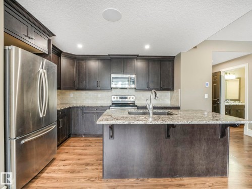 Kitchen featuring dark wood-finish cabinetry, granite countertops, stainless steel appliances, a center island with an undermount sink, and wood-finish flooring - 2807 Wheaton Drive, Edmonton, AB 