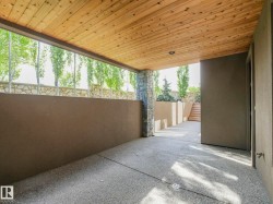 Covered patio featuring a wood-plank ceiling with recessed lighting, exposed aggregate flooring, and a stacked stone column - 