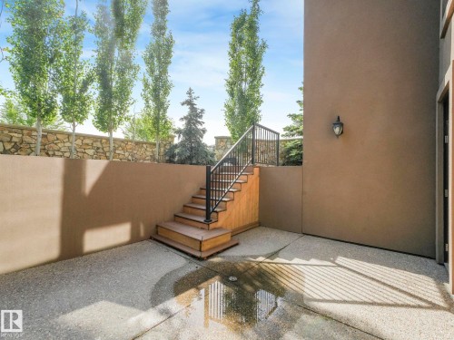 Outdoor patio space featuring an exposed aggregate concrete surface, stucco exterior wall, and a staircase with wood treads and black metal railings - 2807 Wheaton Drive, Edmonton, AB 