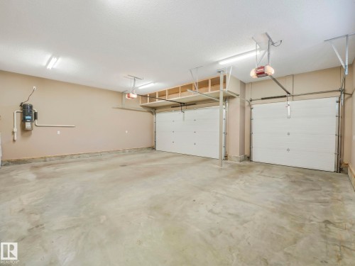 Spacious garage featuring two overhead doors with automatic openers, overhead storage shelving, fluorescent lighting fixtures, and a central vacuum system - 2807 Wheaton Drive, Edmonton, AB 