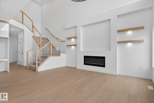 Open-concept living space featuring wood-finish flooring, a contemporary electric fireplace, and built-in shelving with integrated lighting - 105 Wyatt Ridge, Fort Saskatchewan, AB 