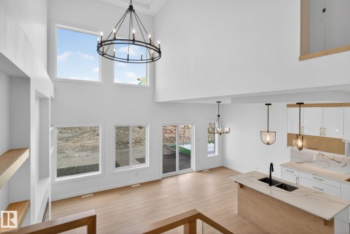 Two-story living area with high ceilings, large windows, light wood-finish flooring, and a modern chandelier - 105 Wyatt Ridge, Fort Saskatchewan, AB 