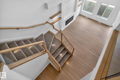 Interior featuring a contemporary staircase with glass panel railings and light wood handrails, carpeted steps, and wood-finish flooring - 105 Wyatt Ridge, Fort Saskatchewan, AB 