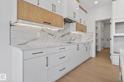 Modern kitchen featuring white cabinetry with gold-tone hardware, wood-finish accent cabinets, and under-cabinet lighting - 105 Wyatt Ridge, Fort Saskatchewan, AB 