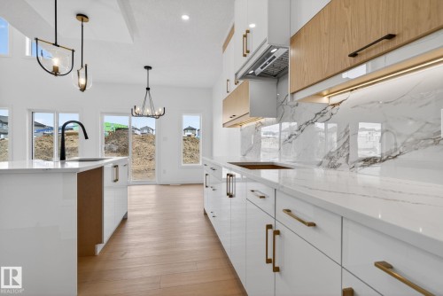 Modern kitchen featuring white high-gloss cabinetry with gold-tone hardware, wood-finish upper cabinets, and a white countertop with a matching backsplash - 105 Wyatt Ridge, Fort Saskatchewan, AB 