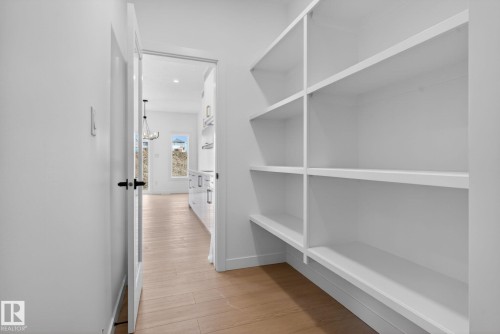 Walk-in pantry featuring extensive built-in shelving, light wood-finish flooring, and a white interior - 105 Wyatt Ridge, Fort Saskatchewan, AB 