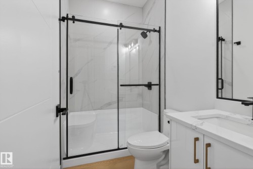 Modern bathroom featuring a glass-enclosed shower with matte black hardware, white vanity with stone-finish countertop, and wood-finish flooring - 105 Wyatt Ridge, Fort Saskatchewan, AB 