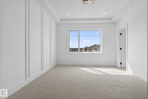 Bright interior space featuring a tray ceiling with recessed lighting, a modern rectangular light fixture, and a large window - 105 Wyatt Ridge, Fort Saskatchewan, AB 