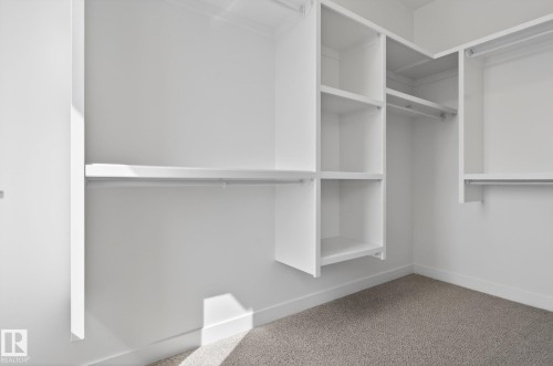 Custom-built closet system featuring integrated shelving, multiple hanging rods, and a neutral carpeted floor - 105 Wyatt Ridge, Fort Saskatchewan, AB 
