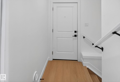Entryway featuring wood-finish flooring, a white paneled door with matte black hardware, and a staircase with a white handrail and black brackets - 105 Wyatt Ridge, Fort Saskatchewan, AB 