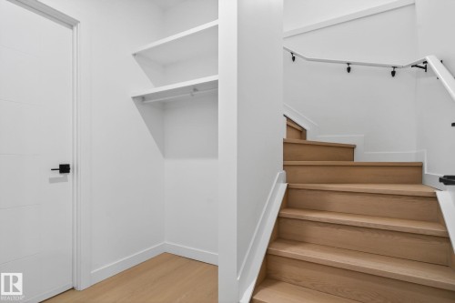 Staircase featuring wood-finish treads and risers, a white handrail with black supports, and a white paneled door with matte black hardware - 105 Wyatt Ridge, Fort Saskatchewan, AB 