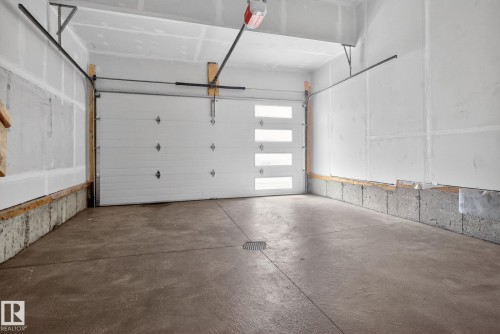 Spacious garage featuring a modern sectional overhead door with frosted glass panels, durable concrete flooring, and a floor drain - 105 Wyatt Ridge, Fort Saskatchewan, AB 