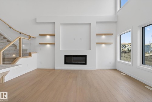 Living area with light wood-finish flooring, a contemporary fireplace, and an integrated media wall with illuminated floating shelves - 105 Wyatt Ridge, Fort Saskatchewan, AB 