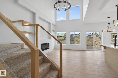 Open-concept living area featuring a two-story ceiling, light wood-finish flooring, and a modern fireplace - 105 Wyatt Ridge, Fort Saskatchewan, AB 